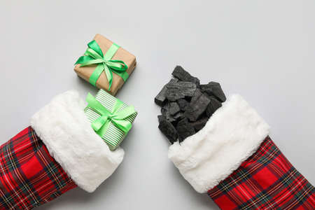 Christmas socks with coal and gift boxes on light background