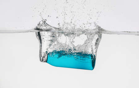 Bottle of cosmetic product in water with splashes on white background