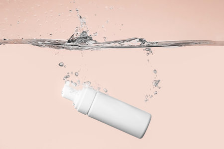 Bottle of cosmetic product in water with splashes on color backgroundの写真素材