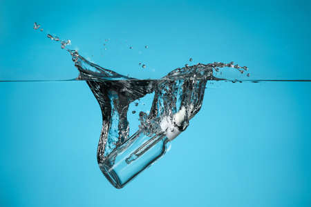 Bottle of essential oil in water on color backgroundの写真素材