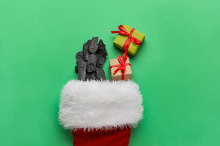 Christmas sock with coal and gift boxes on color backgroundの写真素材