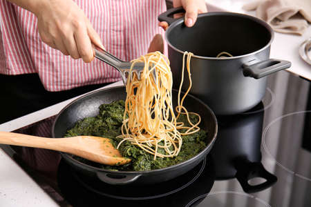 Woman cooking tasty pasta with spinach in kitchen