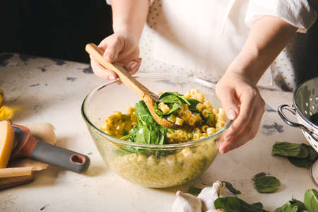 Woman cooking tasty pasta with spinach at table