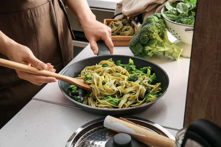 Woman cooking tasty pasta with vegetables in kitchenの写真素材