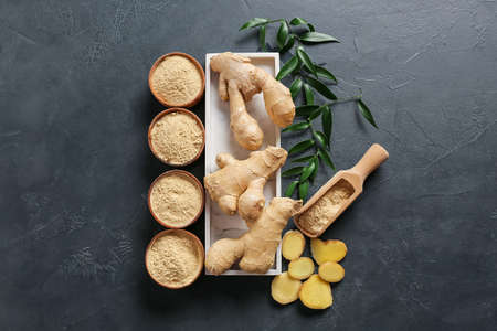 Bowls with ginger powder and roots on dark background