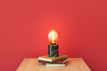 Glowing lamp and books on table near color wall