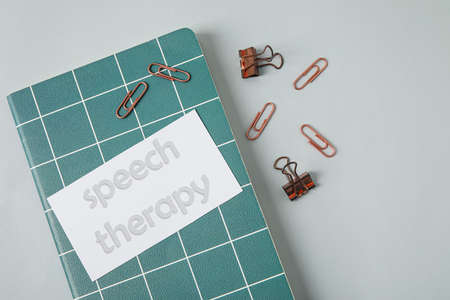 Notebook and paper with text SPEECH THERAPY on light background