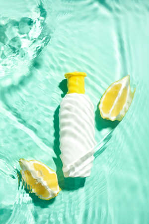 Bottle of cosmetic product and lemon in water on color background