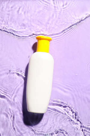 Bottle of cosmetic product in water on color background
