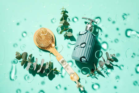 Massage brush, bottle of cosmetic product and eucalyptus branches in water on color background