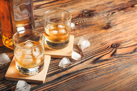 Bottle and glasses of cold whiskey on wooden background