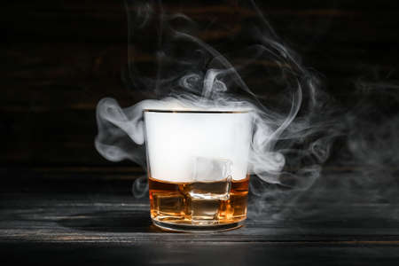 Glass of cold whiskey and smoke on dark wooden backgroundの写真素材