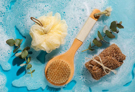 Spa supplies and eucalyptus branches in water with foam on color backgroundの写真素材