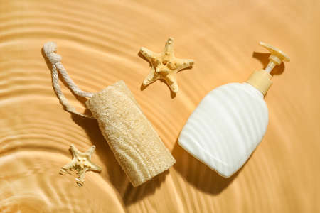 Bottle of cosmetic product, loofah and starfishes in water on color backgroundの写真素材