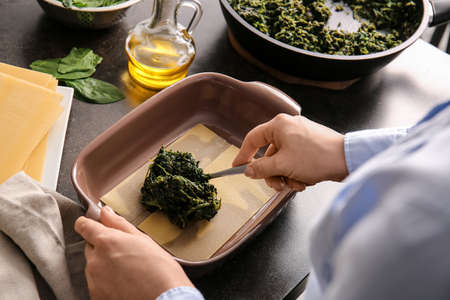 Woman preparing tasty green lasagna in kitchen, closeup