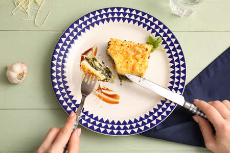 Woman eating tasty green lasagna on color wooden backgroundの写真素材