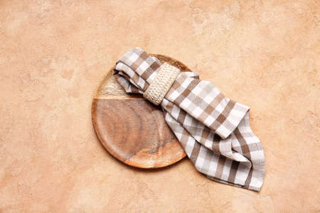 Fabric napkin and wooden plate on color background