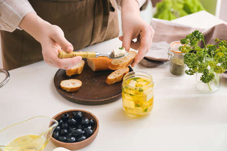 Woman making tasty bruschettas with feta cheese on table in kitchen, closeup