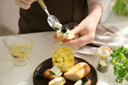 Woman making tasty bruschettas with feta cheese on table in kitchen, closeupの写真素材