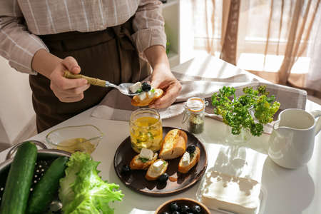 Woman making tasty bruschettas with feta cheese on table in kitchen, closeupの写真素材