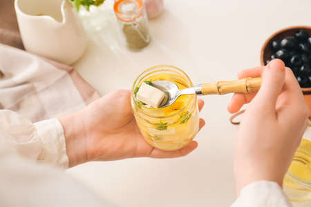 Woman taking piece of tasty feta cheese from jar on table in kitchen, closeupの写真素材