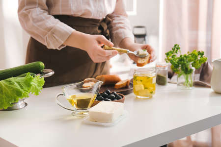 Woman making tasty bruschettas with feta cheese on table in kitchen, closeupの写真素材