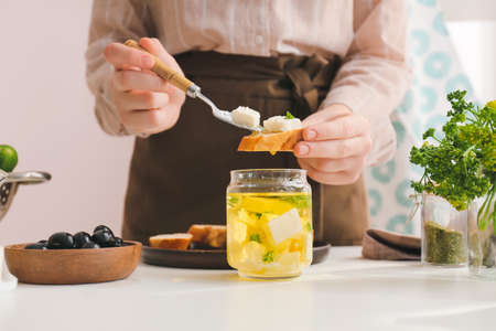 Woman making tasty bruschettas with feta cheese on table in kitchen, closeup