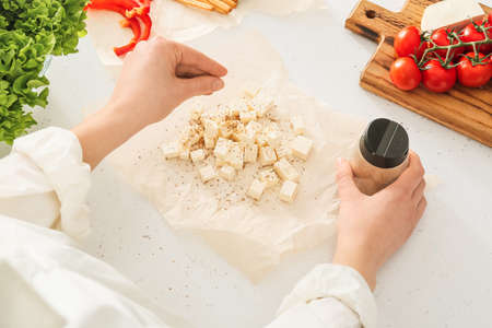 Woman putting spices into cut feta cheese on table in kitchen