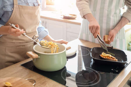 Young couple cooking tasty fish and pasta in the kitchenの写真素材