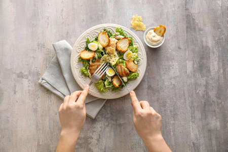 Woman eating tasty Caesar salad on grunge backgroundの写真素材