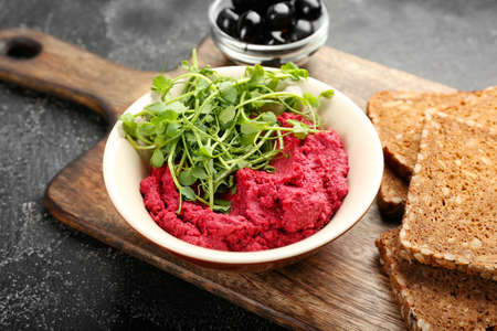 Board with tasty beet hummus, fresh sprouts, olives and bread on dark background