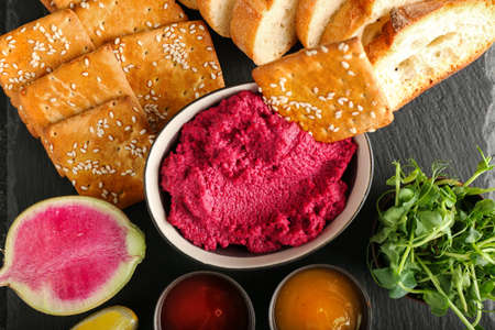 Bowl with tasty beet hummus, bread, crackers, fresh sprouts and sauces on dark background, closeupの写真素材