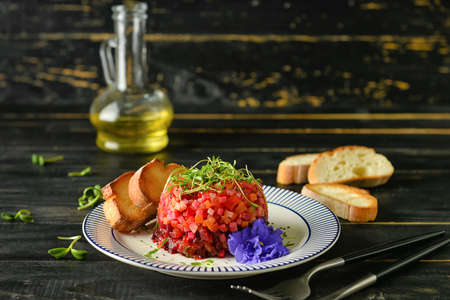 Plate with tasty tartare salad, toasted bread and flower on dark wooden backgroundの写真素材