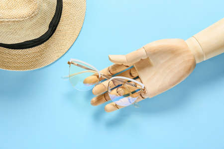 Wooden hand with stylish eyeglasses on color background