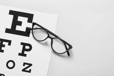 Stylish eyeglasses with eye test chart on light background, closeupの写真素材