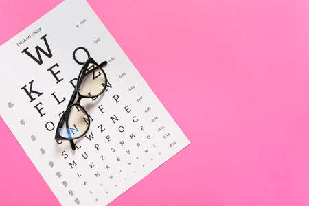 Stylish eyeglasses with eye test chart on color background