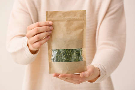 Woman holding paper bag with dried green tea leaves on light background, closeupの写真素材