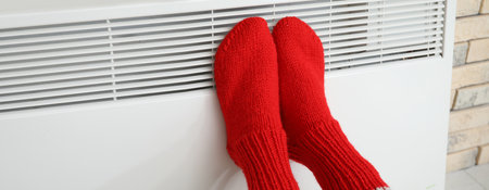 Woman in knitted socks warming her feet at radiator at home. Concept of heating seasonの写真素材
