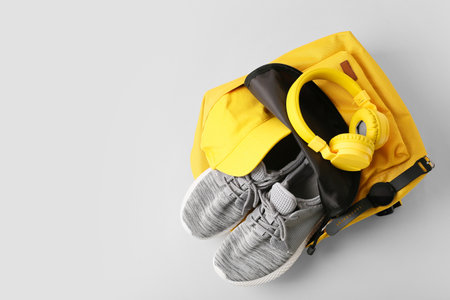 Backpack with sport shoes, headphones and smart watch on gray background