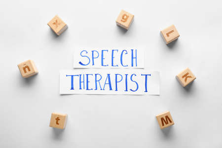 Paper with text SPEECH THERAPIST and cubes on white background