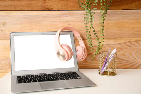 Laptop with headphones on table near wooden wall