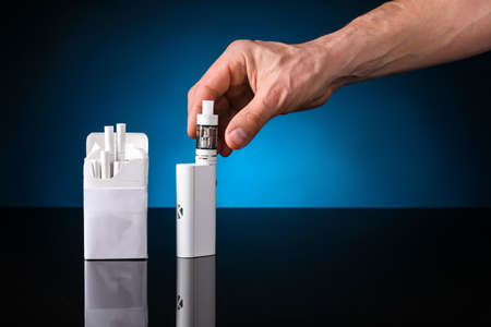 Male hand with vape mod and cigarettes in box on dark background