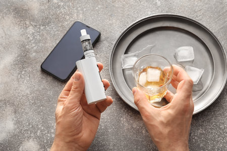 Man with vape mod and glass of whiskey at table