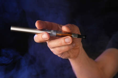 Male hand with electronic cigarette on dark background with fumeの写真素材