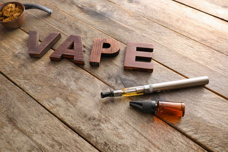 Electronic cigarette with oil and word VAPE on wooden background