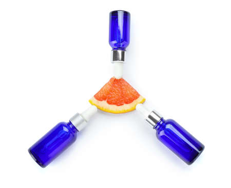 Bottles of essential oil and slice of grapefruit on white background