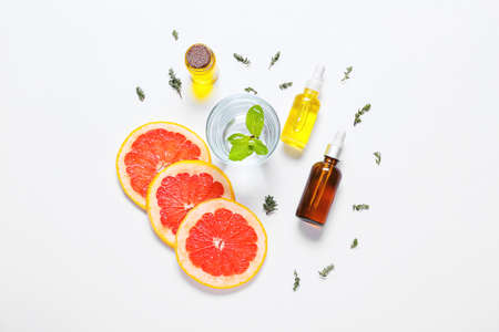 Composition with bottles of essential oil, glass of water and grapefruit slices on light background