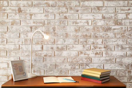 Table with books and glowing lamp near brick wallの写真素材
