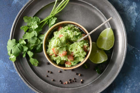 Bowl with tasty guacamole and lime on color background