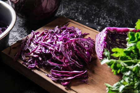 Board with cut fresh purple cabbage on dark background, closeup
